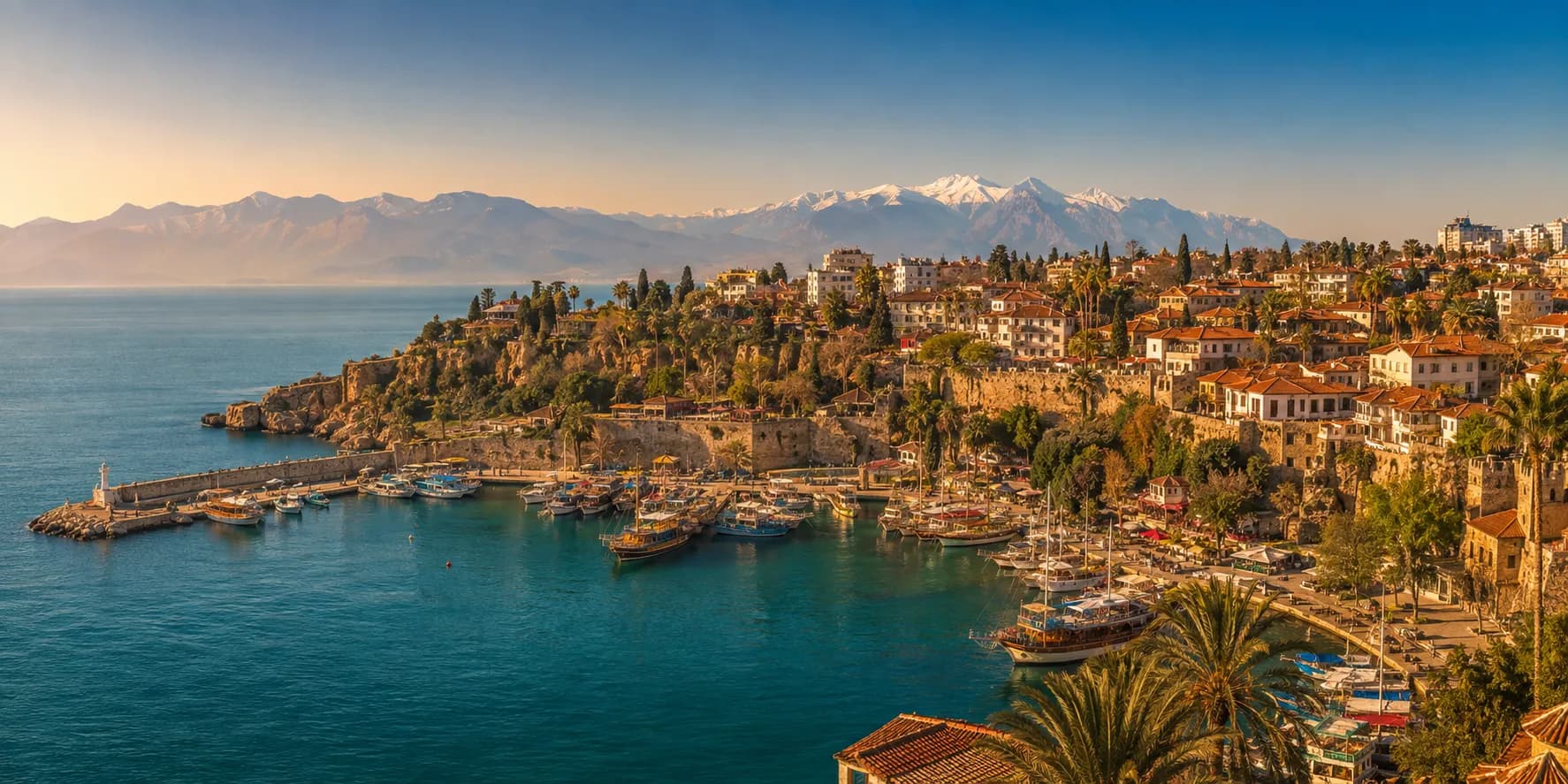 Antalya's Kaleiçi old harbour with moored boats, the old town on the cliffs above and the snow-capped Taurus Mountains beyond