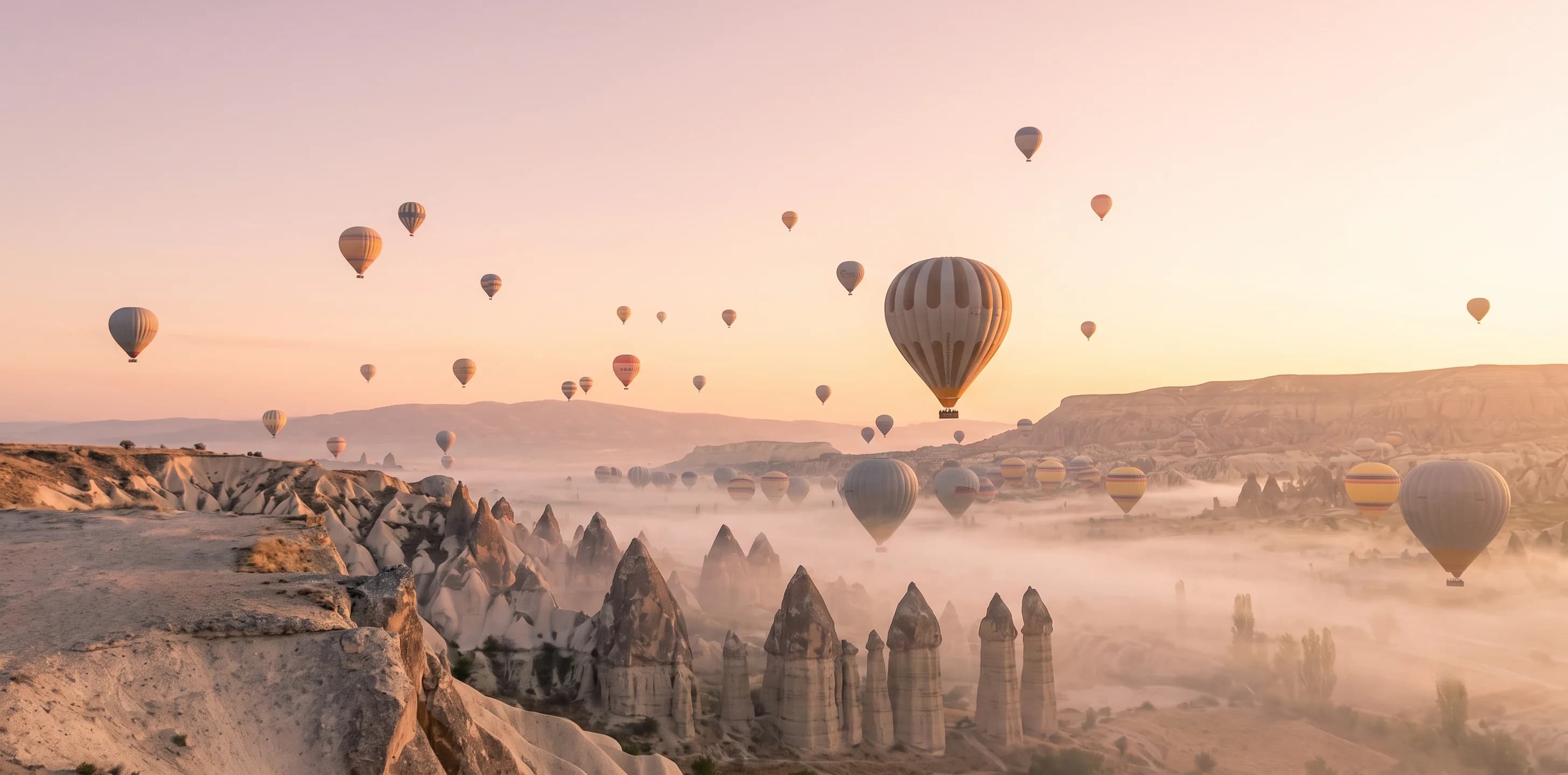 Hot air balloons flying over Cappadocia's fairy chimney valleys at sunrise, Turkey