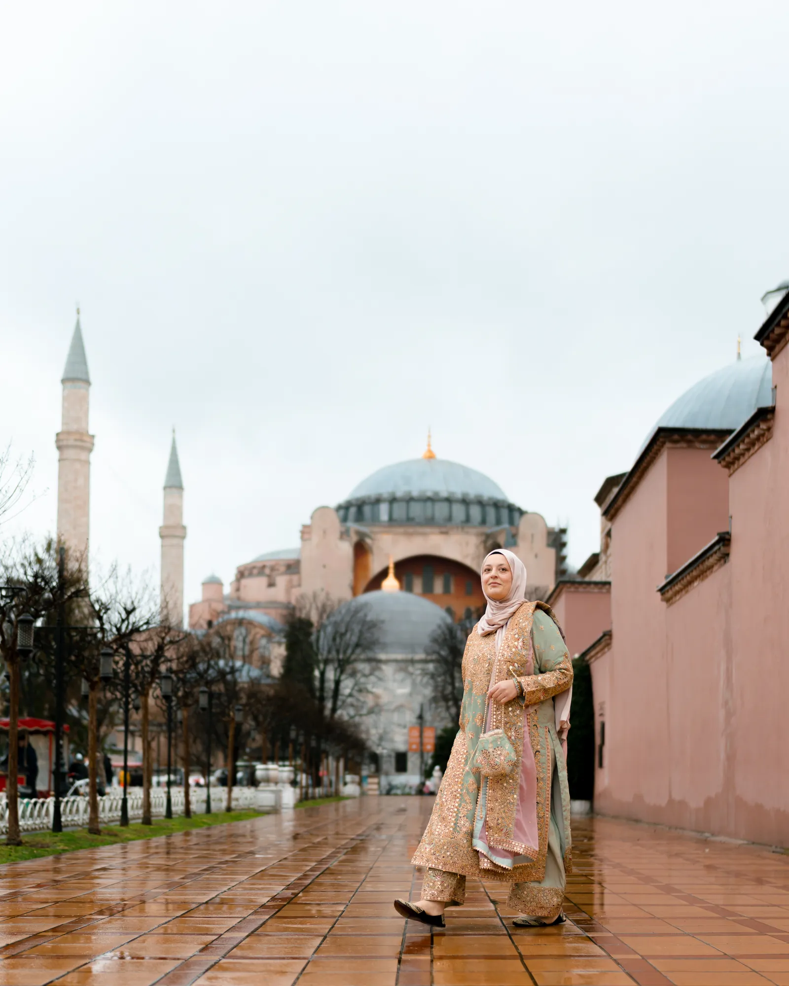 Türkan Atay walking past Hagia Sophia after rain, its domes and minarets rising behind her