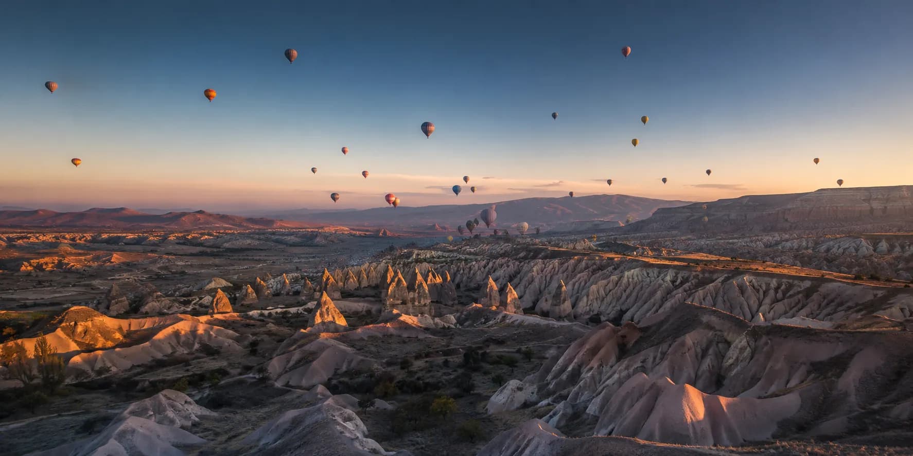 Hot air balloons drifting at dawn above the fairy chimneys and eroded valleys of Cappadocia