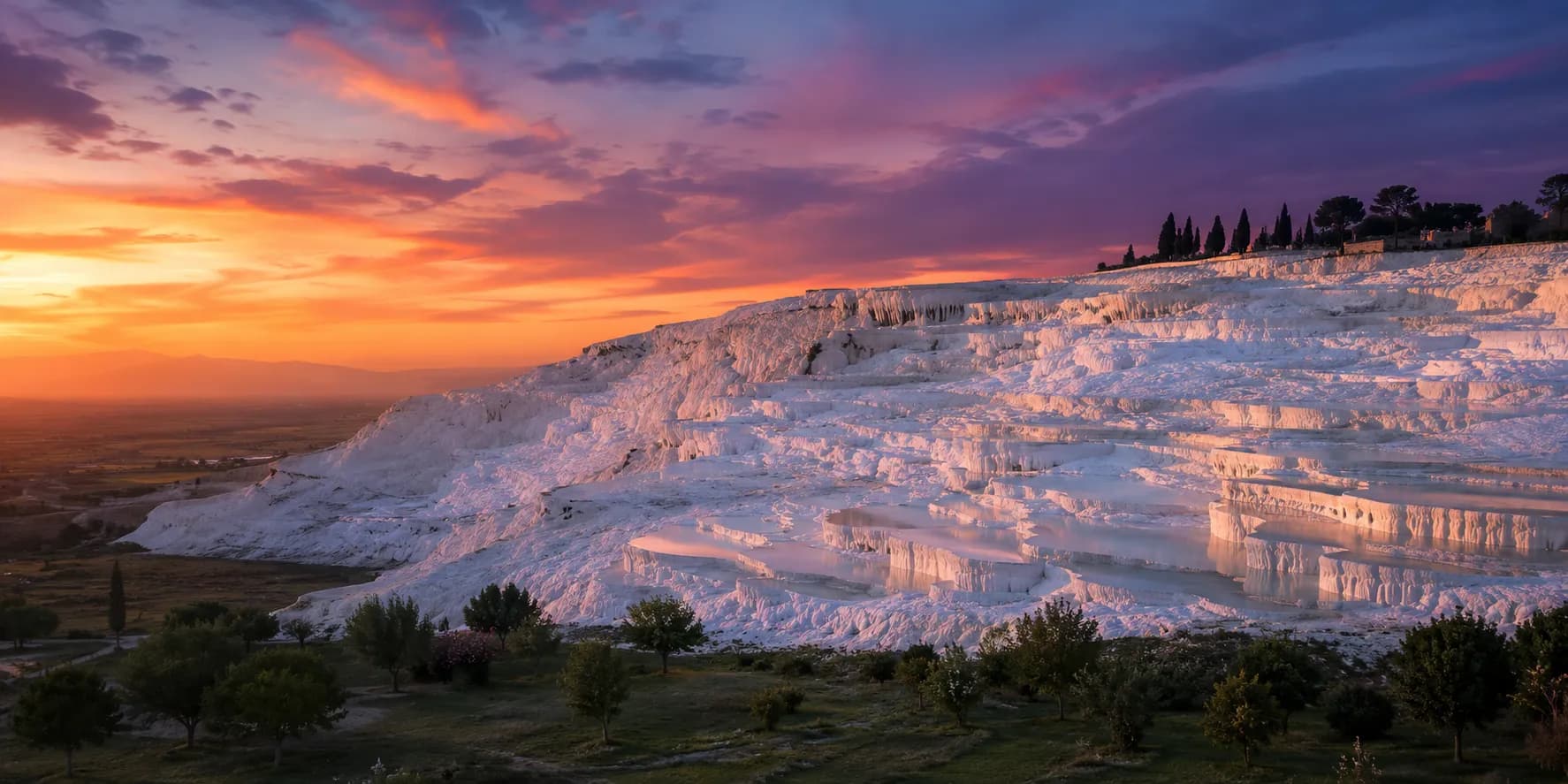 The white travertine terraces of Pamukkale glowing beneath a purple and orange sunset sky
