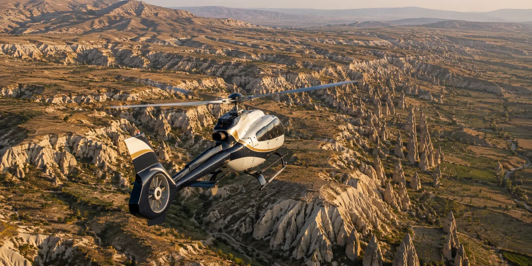 A helicopter banking over the fairy chimneys and ravines of Cappadocia in late afternoon light
