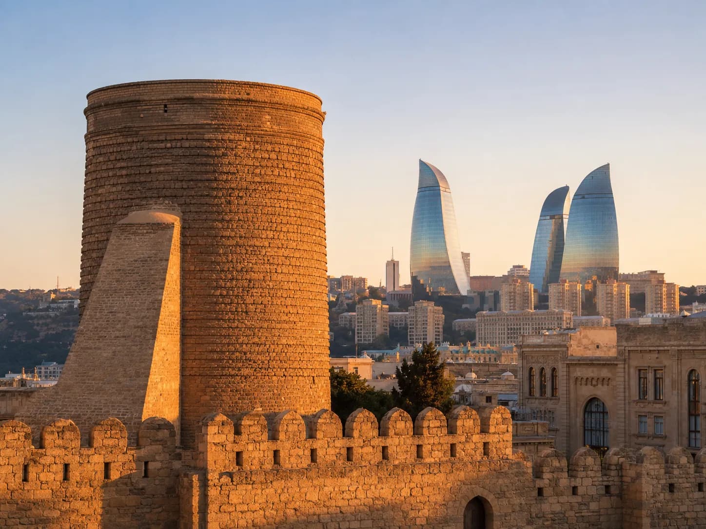 The Maiden Tower and the walls of Baku's old city at sunset, with the three Flame Towers on the skyline behind