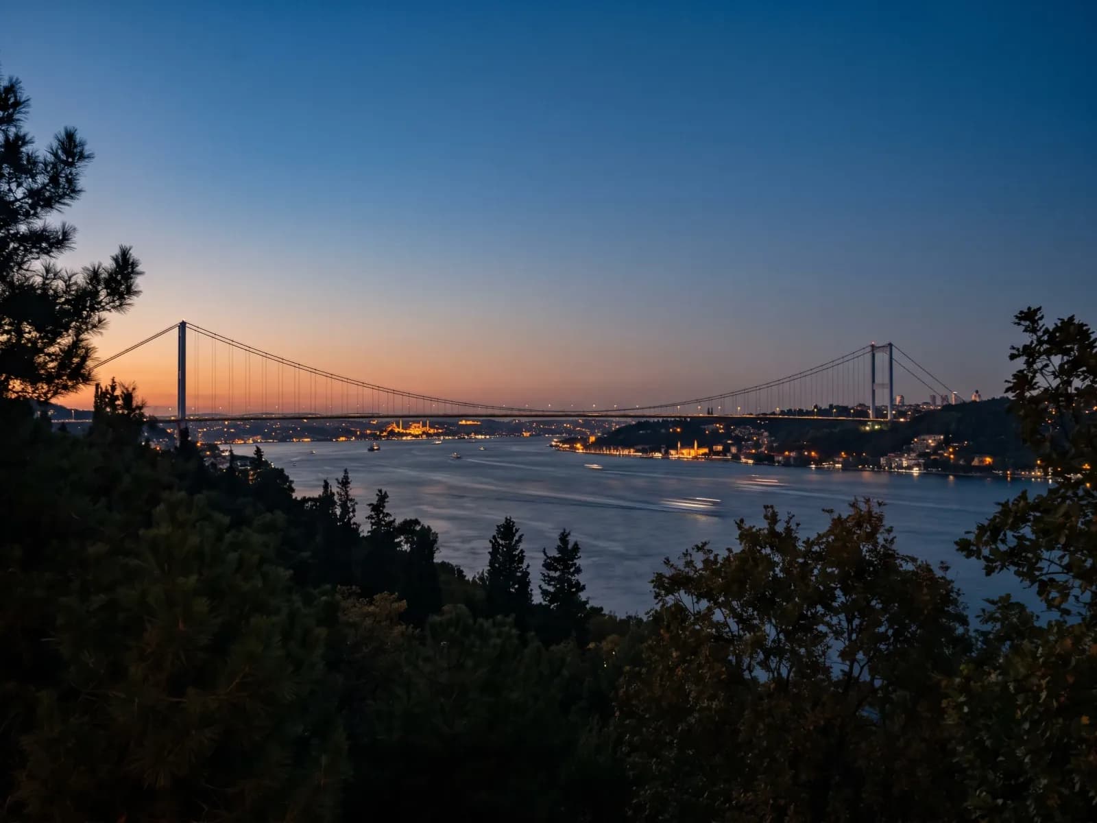 The Bosphorus suspension bridge lit at dusk, spanning the strait between Europe and Asia